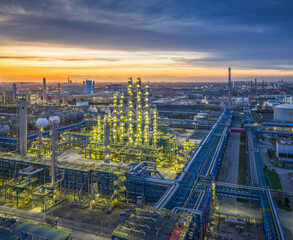 A brightly illuminated chemical processing unit at a large oil refinery complex during the twilight hours after sunset.