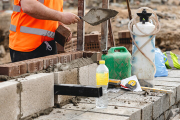 Construction worker laying bricks at a building site during daylight hours using various tools and materials for masonry tasks