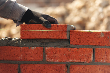 Skilled worker laying red bricks in a construction site during daylight with focused attention on building a wall