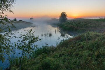 rising sun over the foggy river and field 