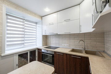 Modern kitchen with white cabinets, dark wood lower cabinets, and a beige countertop. Window with blinds on the left