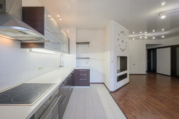 Modern kitchen open to living space. Features sleek cabinets, white tiles, and a decorative wall with a clock