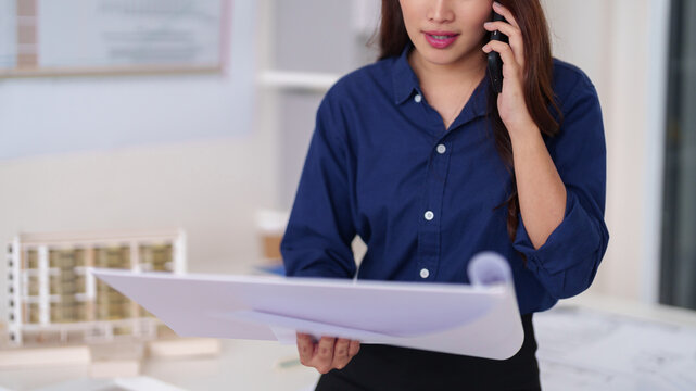 Asian woman architect professional discusses building design plans via smartphone client collaboration modern architectural office studio construction project management