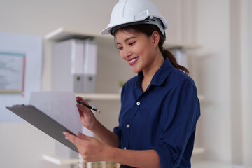 Asian woman architect engineer professional reviews construction plans project designs meticulously smiling confidently in modern office site development workspace