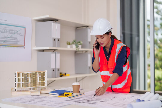 Asian adult architect engineer professional woman busy calling drawing blueprints project plans design office construction site development