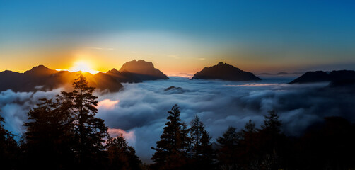Sun rising behind mountain peaks, high above the clouds, 