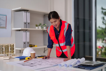 Asian female architect engineer reviews construction blueprints plans project details professional building development in modern office workspace