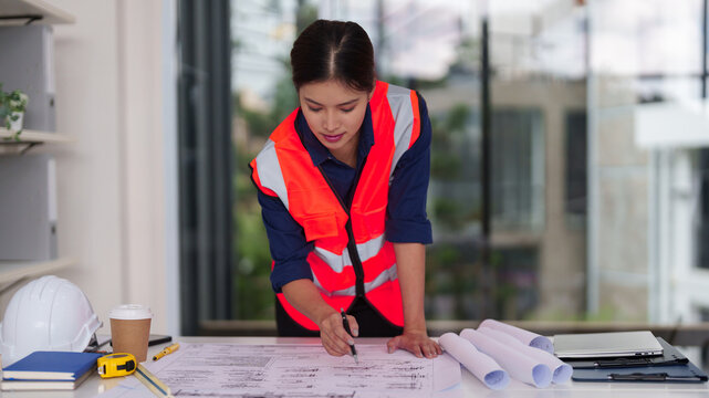 Asian female architect engineer construction professional reviewing architectural blueprints project plans inspecting design details modern office workspace - Powered by Adobe