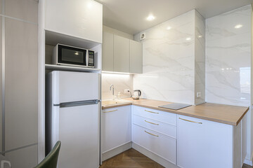 bright, modern kitchen with white cabinets, marble-look backsplash, wood countertops, and stainless steel appliances