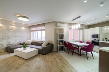 modern open-concept living and dining area with a gray sectional, white table, and purple dining chairs. The kitchen has white cabinets