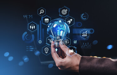Hand holding glowing bulb with digital icons representing innovation, idea, and business analytics on futuristic dark blue background concept.