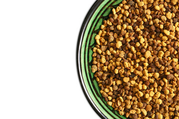 Bee pollen granules in a green striped bowl. Healthy natural supplement with vibrant golden color. Organic texture on white background. Superfood for energy vitality and nutrition. Natural medicine.