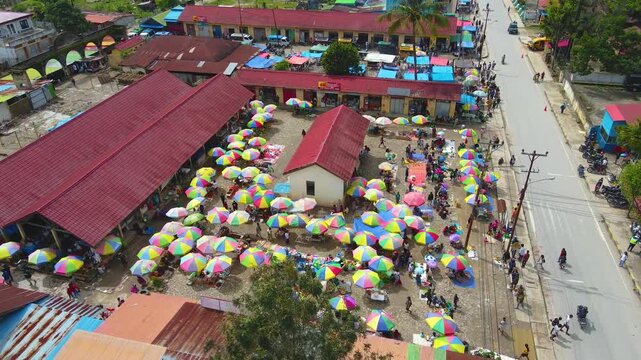 A lively aerial view of the traditional market in Aileu, Timor-Leste. Hundreds of colorful umbrellas belonging to vendors create a vibrant pattern amid the hustle and bustle of buying and selling.