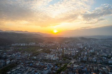Naklejka premium Aerial view captures Wudang town in China, with many buildings, bathed in warm sunset light against scenic mountains.