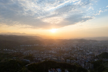 Warm sunlight bathes Wudang town in China, creating a serene landscape over mountains and buildings at sunset with soft clouds.