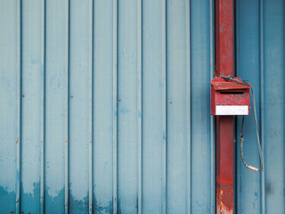 Blue sheet metal walls with grooves and a red square tube steel post with a mail box mounted.
