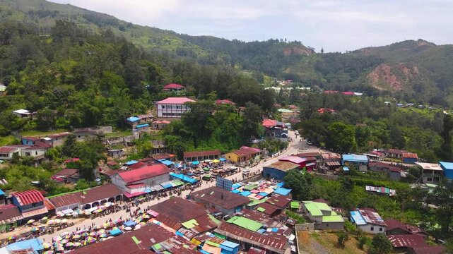 A stunning aerial view of Maubisse, a beautiful mountain town in Timor-Leste. A bustling traditional market blends with the residential settlement amidst a lush, hilly landscape.