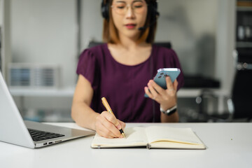 Serious call center operator in wireless headset talking to customer, woman in headphones with microphone consulting customer on phone in customer support service, looking at computer screen.
