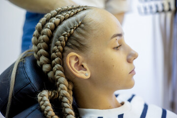 Young girl undergoing a braiding transformation in a stylish hair salon during daylight hours