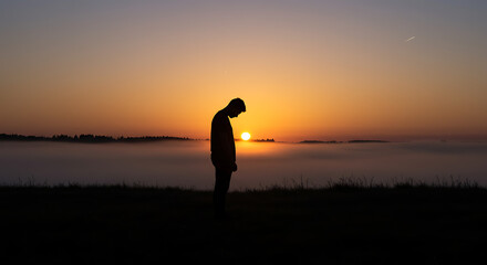 Fototapeta premium Silhouette Of A Man Standing On A Hill At Sunrise In A Foggy Landscape
