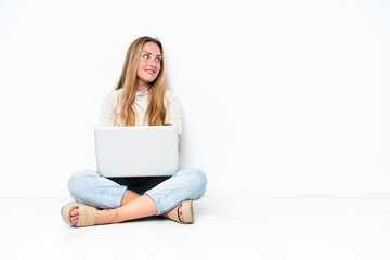 Fototapeta premium Young woman with laptop sitting on the floor isolated on white background with arms crossed and happy