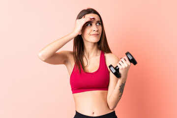 Young sport woman making weightlifting over isolated pink background having doubts and with confuse...