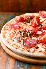 Pizza with ham, salami, tomatoes and mozzarella cheese. Rustic wooden background. Soft focus. Close up.	