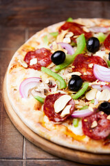 Pizza with chorizo ​​sausage, mozzarella cheese, green pepper and black olives. Rustic wooden background. Soft focus.	
