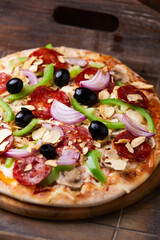 Pizza with chorizo ​​sausage, mozzarella cheese, 
green pepper and black olives. Rustic wooden background. Soft focus. 