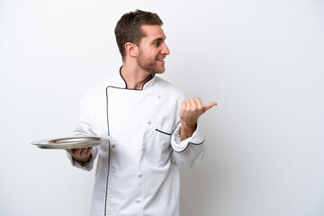 Young caucasian chef with tray isolated on white background pointing to the side to present a product