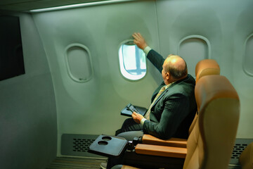Overweight white male business traveler sitting at airplane window, holding smartphone and open window. Perfect for airline service, aviation industry, in-flight lifestyle, tourism.