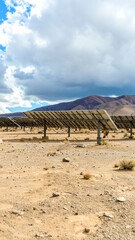 Rows of solar panels in a desert landscape under a cloudy sky