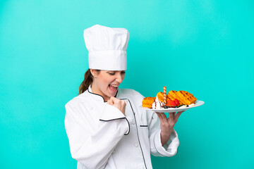 Young caucasian chef woman holding waffles isolated on blue background celebrating a victory