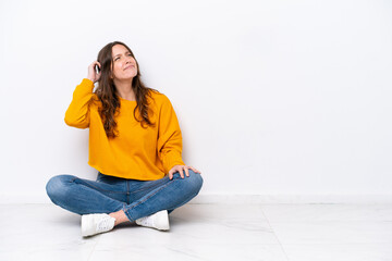 Young caucasian woman sitting on the floor isolated on white wall having doubts and with confuse face expression