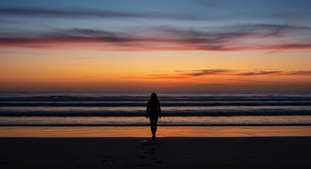Solitary Silhouette: Woman Walks on Beach at Sunset with Vibrant Sky