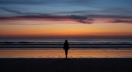 Contemplative Twilight Walk: A Woman's Silhouette on a Beach at Colorful Sunset.