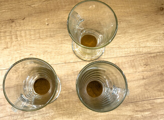 Instant coffee powder in three clear glass mugs with handles on a wooden table, ready to be prepared with hot water.