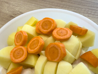 Closeup of chopped carrots and potatoes in a bowl, fresh root vegetables prepared for cooking soup, stew, or other meals.