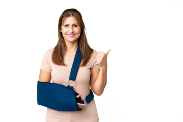 Middle age with broken arm and wearing a sling over isolated background pointing to the side to present a product