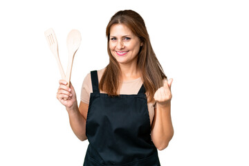 Middle age caucasian woman holding a rolling pin over isolated background making money gesture