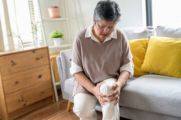 Mature Asian female suffering from knee pain osteoarthritis. Close up senior woman holding her knee...