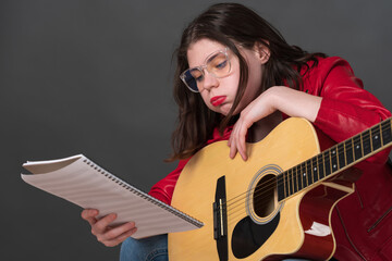 Female musician, equipped with guitar, meticulously examines sheet music while exhibiting countenance indicative of exhaustion during protracted and arduous rehearsal