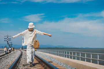 Happy asian traveler woman with white hat relax and walk in railway with lake and blue sky background in Pa Sak dam Lopburi Thailand Summer travel vacation holiday concept
