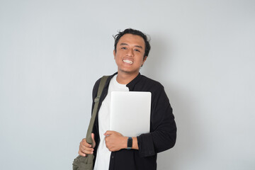 Asian man smiling while carrying laptop and shoulder bag. Concept of student, working lifestyle, technology, and modern digital professional on white background.