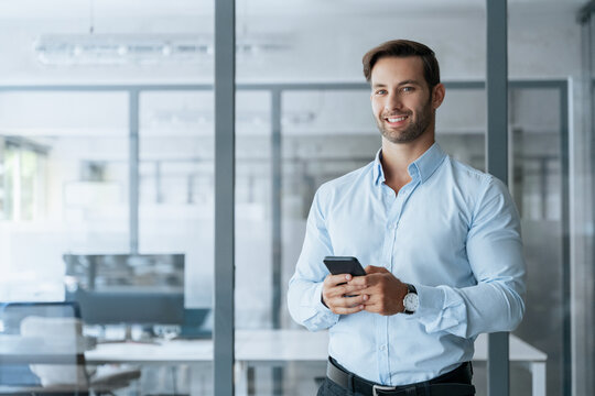 Young European business man manager ceo using cell phone mobile app. Latin Hispanic male businessman holding smartphone in office for trading, reading, working online, smiling at camera. Copy space