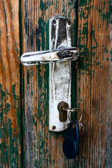 Scratched, rough green painted door with dirty white door handle and keys.
