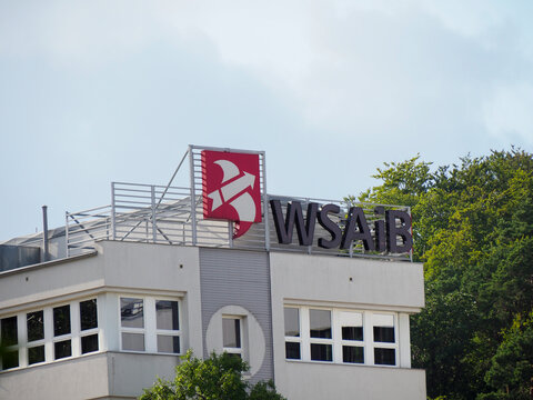 The exterior of the WSB University building with a prominent red logo against a cloudy sky in Gdynia, Poland.