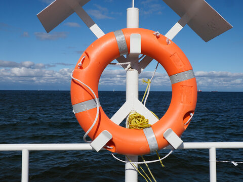 A vibrant orange lifebuoy on a boat deck with the expansive blue ocean and a clear horizon behind.