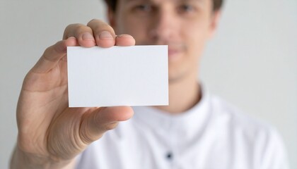 Close up selective focus on a blank white business card held by a male professional, ideal mockup for contact information or branding