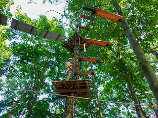 A person in a helmet and harness hanging from a rope, preparing to descend from a high wooden platform in a forest ropes course.